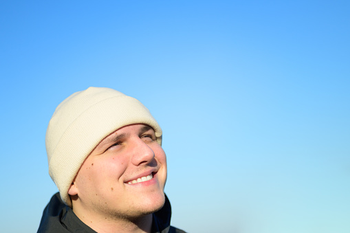 Happy young man enjoying the autumn sunshine looking up into the air with a beaming smile of pleasure in a closeup headshot against blue sky