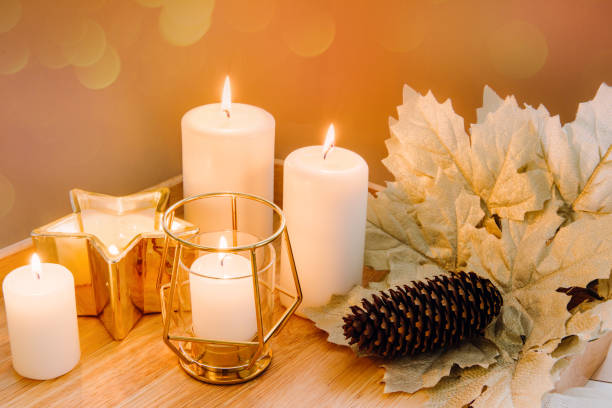 istock Autumn composition. Candles, golden maple leaves and pine cone on beige background. Glare from burning candles. Selective focus. 1289401943