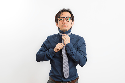 Middle age Asian man in black shirt dressing up and adjusting tie on neck standing on white background.