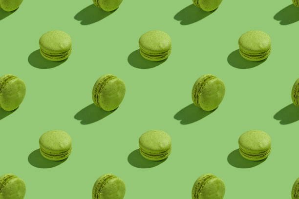 istock Green macaroons with shadows on colored background. Trendy minimal seamless pattern. French cookies macarons on a green background. Delicious healthy french dessert. Creative modern background 1289402766