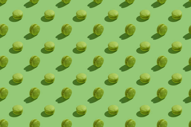 istock Green macaroons with shadows on colored background. Trendy minimal seamless pattern. French cookies macarons on a green background. Delicious healthy french dessert. Creative modern background 1289402784