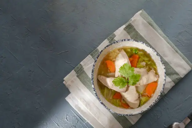 Photo of Snakehead fish porridge topped with coriander in a bowl on gray table. rice soup with sliced fish. Congee or conjee is a type of rice porridge or gruel popular in many Asian countries.