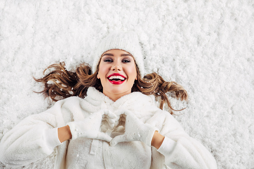Girl lying down on the snow showing love sign