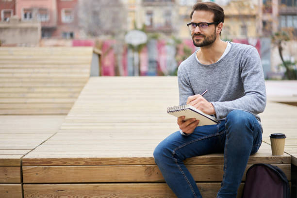 istock Handsome young concentrated male journalist taking notes in notebook while sitting in street 1289403700