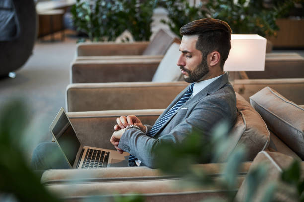 istock Attractive young man touching his watch while sitting in the armchair 1289408004