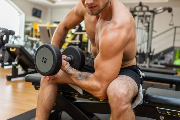 istock Muscular man training biceps with concentration while sitting on bench in gym 1289409170