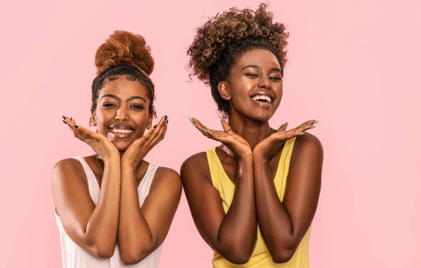 Happy overjoyed two afro women smile broadly Happy overjoyed two afro women smile broadly, looking at camera, posing on pink pastel studio background. charming photos stock pictures, royalty-free photos & images