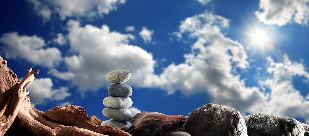 dramatic landscape of dried tree trunk and stones over sunny and cloudy blue sky