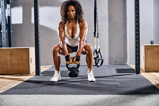 Front view of a woman lifting the single kettlebell off the ground with two arms