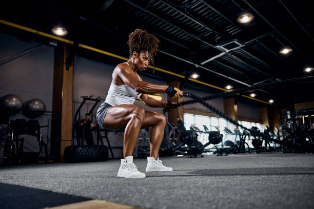 Athletic woman doing the full-body cardio workout Motivated strong sporty lady performing the alternating waves exercise with battle ropes at the gym muscle stock pictures, royalty-free photos & images
