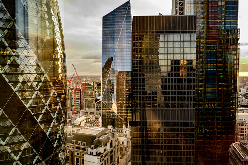 Unusual partial view of landmark glass and steel office buildings in financial district with construction cranes and sprawling city in background at dusk.