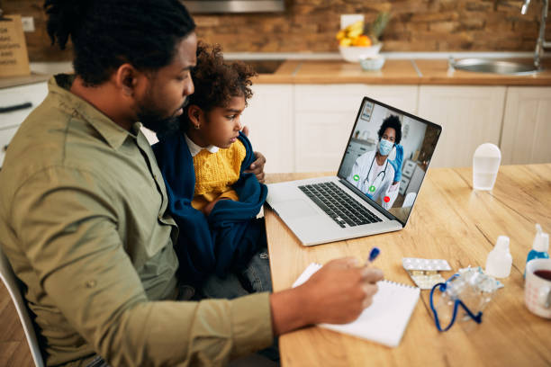African American father and daughter having video call with family doctor due to coronavirus pandemic. Black father and daughter communicating with a doctor via video call from home during COVID-19 pandemic. Focus is on girl. health technology photos stock pictures, royalty-free photos & images