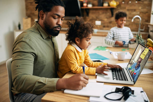 istock Black working father having video conference and taking notes while babysitting his kids at home. 1289420443