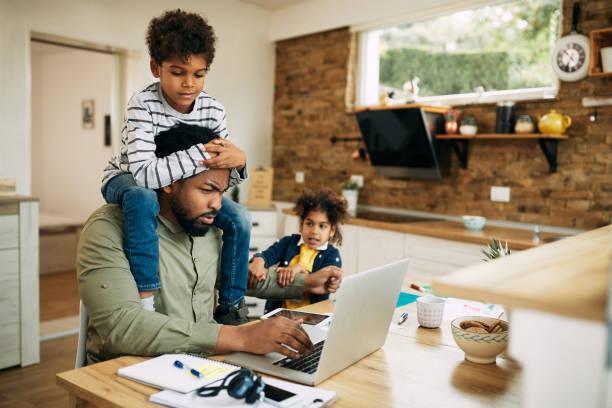 los negros se quedan en casa padre trabajando en la computadora portátil mientras sus hijos están exigiendo su atención. - angustiado fotos fotografías e imágenes de stock