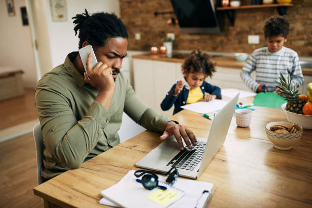 istock Black stay at home father talking on the phone while working on laptop. 1289421255