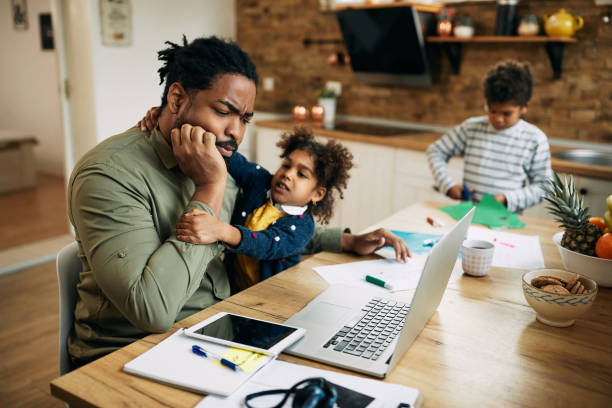 istock Pensive black father working on laptop while daughter is seeking his attention at home. 1289421312