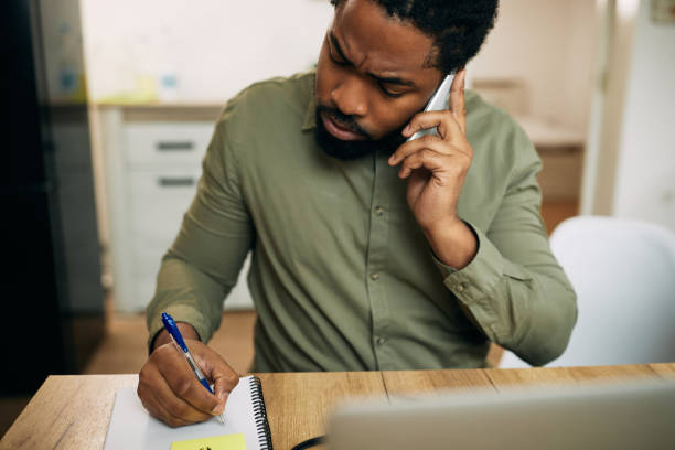 istock African American man talking on the phone and writing notes while working at home. 1289421313