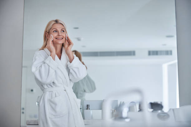 hermosa hembra adulta en blanco felpa albornoz limpieza piel cara en el baño - quartz caucasian one person energy fotografías e imágenes de stock