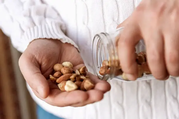 The man is holding a jar of walnuts hazelnuts and almonds