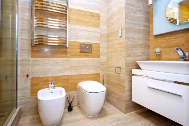 Clean and white toilet and bidet with gold-plated faucet in the beige bathroom