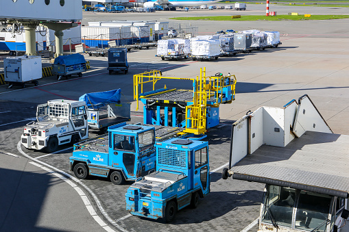 Amsterdam, Netherlands, 30/09/20. Airport ground handling support equipment, vehicles, tugs, stairs, dollies for cargo pallets at Amsterdam Airport Schiphol (AMS), aircraft parked in the background.