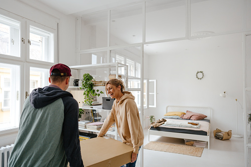 Photo of a young couple moving into a new apartment, carrying boxes and furniture in.