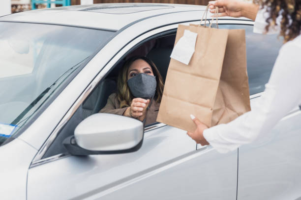 Woman with protective mask drives up to get curbside order The woman with the protective mask stays in her car to pick up a curbside order from a restaurant during the coronavirus outbreak. drive through photos stock pictures, royalty-free photos & images