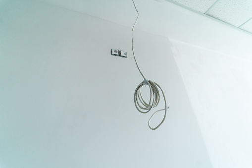 One internet cable hangs from the celing. Newly repaired room. White walls background.