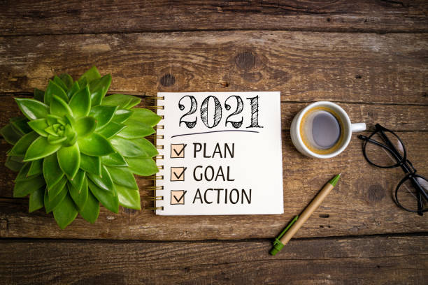 istock New year goals 2021 on desk. 2021 resolutions list with notebook, coffee cup and eyeglasses on wooden background. Goals, plan, strategy, business, idea, action concept 1289440794