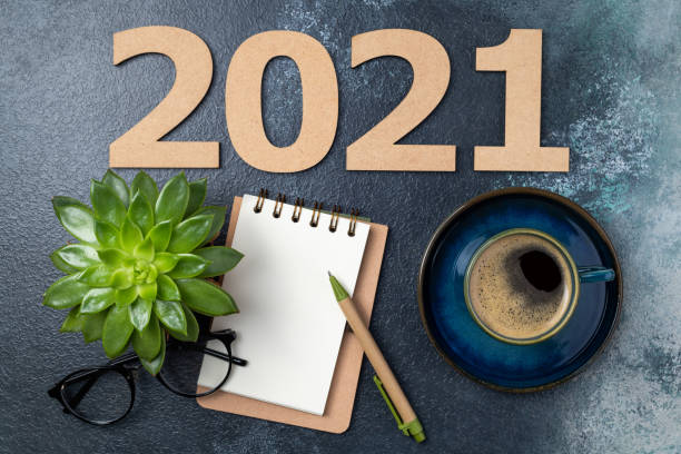 istock New year resolutions 2021 on desk. 2021 goals with open notebook, coffee cup, eyeglasses, plant succulent on blue background. Goals, plan, strategy, action, idea concept. New Year 2021 template 1289440812