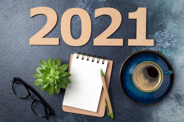 istock New year 2021 and notebook on desk. 2021 template with open notebook, coffee cup, eyeglasses, plant succulent on blue background. Goals, plan, strategy, resolutions, business concept 1289440818