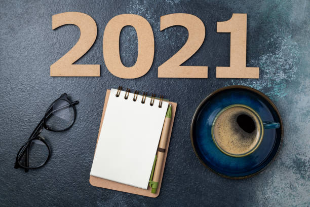 istock New year 2021 and notebook on desk. 2021 template with open notebook, coffee cup, eyeglasses on blue background. Goals, planning, strategy, resolutions, business concept 1289440820