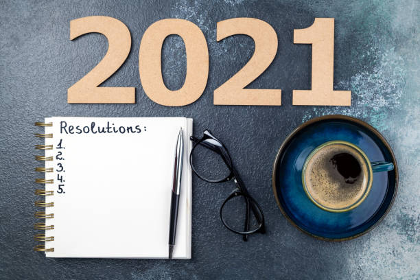 istock New year resolutions 2021 on desk. 2021 resolutions with open notebook, coffee cup, eyeglasses on blue background. Resolutions, goals, planning, strategy, business concept 1289440880