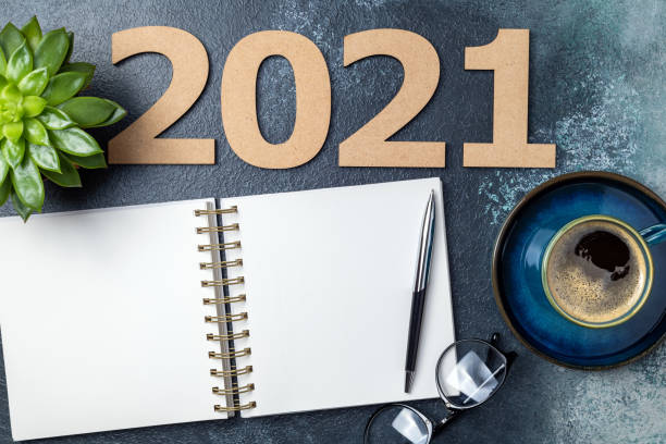 istock New year 2021 and notebook on desk. 2021 template with open notebook, coffee cup, eyeglasses, plant succulent on blue background. Goals, plan, strategy, resolutions, business concept 1289440886