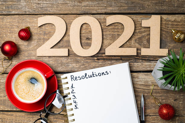 istock New year 2021 resolutions on desk. 2021 goals with notebook, coffee cup, eyeglasses, Christmas decorations on wooden background. Goals, plan, strategy, action, idea concept. New Year 2021 template 1289440989
