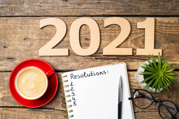 istock New year resolutions 2021 on desk. 2021 resolutions with open notebook, coffee cup, eyeglasses on wooden background. Goals, plan, strategy, action, idea concept. New Year 2021 template 1289441211