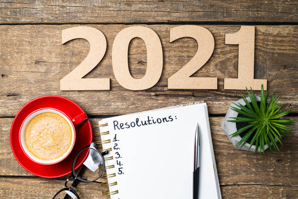istock New year resolutions 2021 on desk. 2021 resolutions with open notebook, coffee cup, eyeglasses on wooden background. Goals, plan, strategy, action, idea concept. New Year 2021 template 1289441699