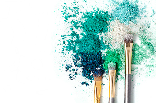 Make-up brushes and powdered cosmetic shadows on a white background. Top view. Text space.