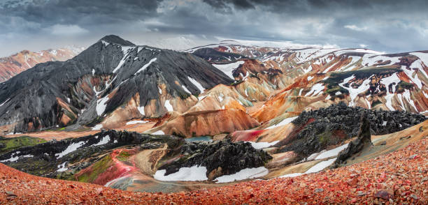 Amazing Icelandic landscape of colorful rainbow volcanic Landmannalaugar mountains, at famous Laugavegur hiking trail with dramatic snowy sky, and red volcano soil in Iceland stock photo