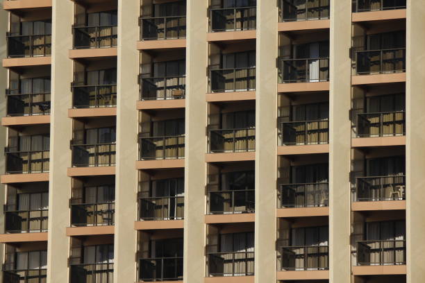 rows of apartments in a large modern building with glass balconies and outdoor furniture and sky reflected in the windows