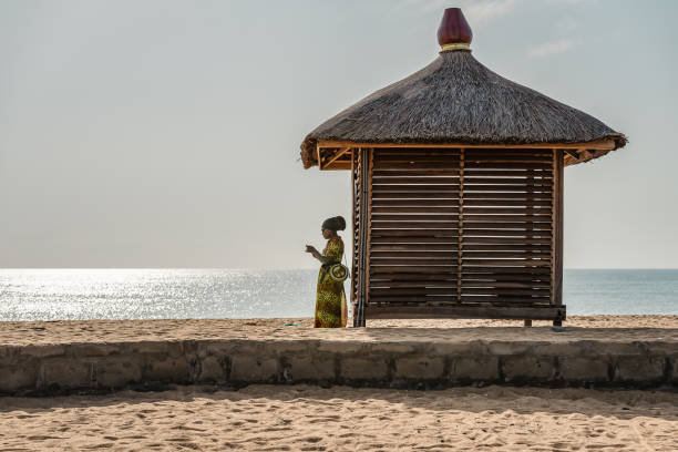African woman standing next to a bungalow alone wearing African clothes on the coast of Africa in Keta Ghana West Africa