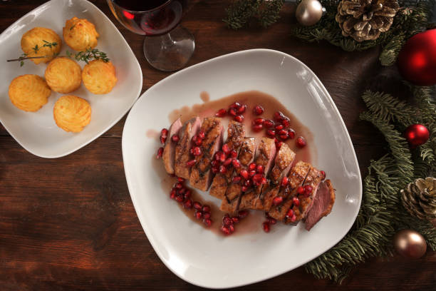 Festive holiday dinner from roasted duck breast with pomegranate seeds and duchess potatoes on a white plate and a dark wooden table with Christmas decoration, high angle view from above Festive holiday dinner from roasted duck breast with pomegranate seeds and duchess potatoes on a white plate and a dark wooden table with Christmas decoration, high angle view from above, selected focus duchess photos stock pictures, royalty-free photos & images