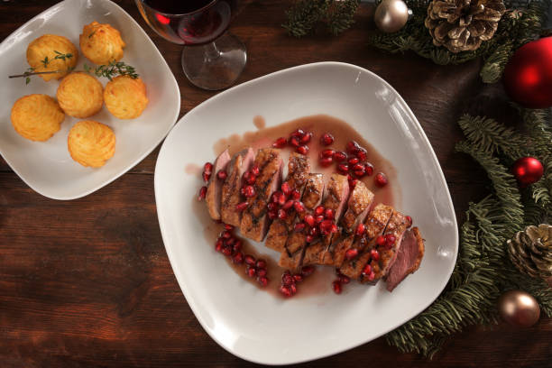 festive holiday dinner from roasted duck breast with pomegranate seeds and duchess potatoes on a white plate and a dark wooden table with christmas decoration, high angle view from above - peerage title imagens e fotografias de stock