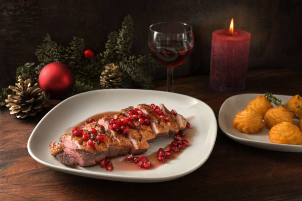 白い皿にザクロの種と公爵夫人のジャガイモとローストアヒルの胸肉、暗い木製のテーブルの上にクリスマスの装飾とお祝いの休日のディナー - duck breast ストックフォトと画像