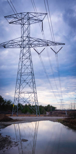 istock Tall electrical pylon with high voltage power lines and reflections on the puddle 1289462282