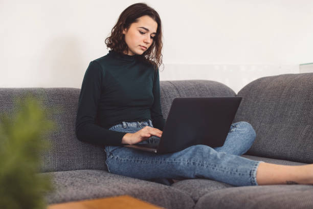 istock Young woman sitting comfortable on the couch writing a school assignment on her laptop 1289468066