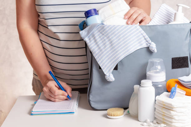 Woman packing diaper bag in maternity hospital. Unrecognizible pregnant caucasian woman in striped t-shirt packing big blue diaper bag to maternity hospital. Diapers, nappy, hat, bottle and other necessary things for newborn baby. 8 months pregnant stock pictures, royalty-free photos & images