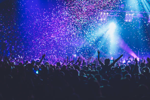 istock A crowded concert hall with scene stage lights, rock show performance, with people silhouette, colourful confetti explosion fired on dance floor air during a concert festival 1289480497
