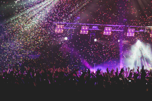 istock A crowded concert hall with scene stage lights, rock show performance, with people silhouette, colourful confetti explosion fired on dance floor air during a concert festival 1289481247