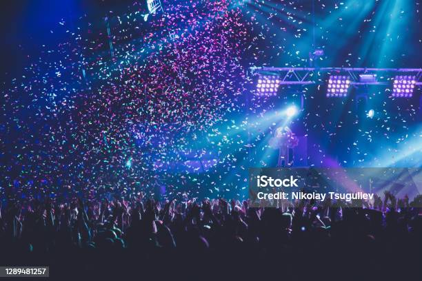 A Crowded Concert Hall With Scene Stage Lights Rock Show Performance With People Silhouette Colourful Confetti Explosion Fired On Dance Floor Air During A Concert Festival Stock Photo - Download Image Now